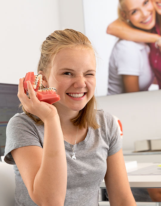 Mädchen in einer Praxis für Kieferorthopädie mit einem Zahnmodell im Hand